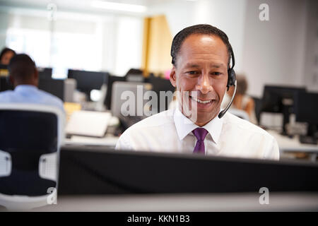Middle aged man working at computer with headset in office Stock Photo