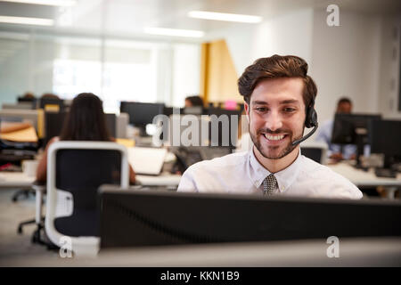 Young man working at computer with headset in busy office Stock Photo