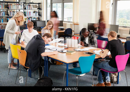 Busy College Library With Teacher Helping Students At Table Stock Photo