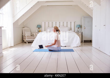 Woman With Digital Tablet Using Meditation App In Bedroom Stock Photo