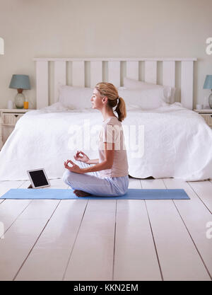 Woman With Digital Tablet Using Meditation App In Bedroom Stock Photo