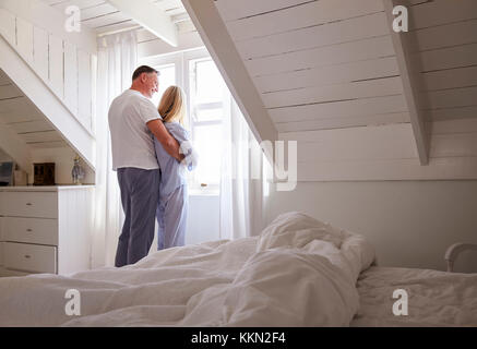 Mature Couple Opening Curtains And Looking Out Of Window Stock Photo