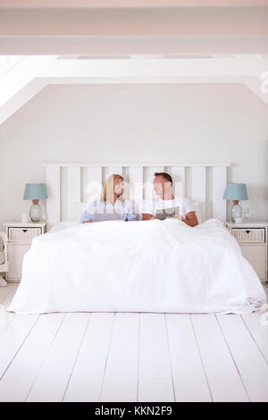 Couple Wearing Pajamas Lying In Bed Using Digital Devices Stock Photo