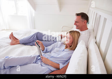 Couple Lying In Bed Looking At Digital Tablet Together Stock Photo