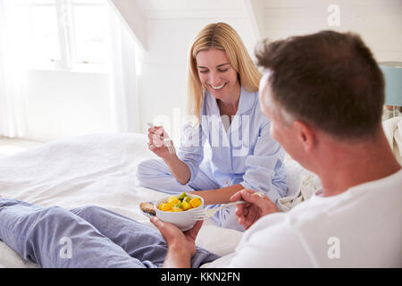 Couple Wearing Pajamas Sitting In Bed Eating Breakfast Together Stock Photo