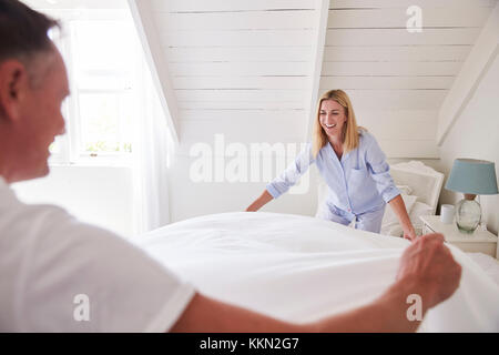Couple Wearing Pajamas Making Bed In Morning Stock Photo