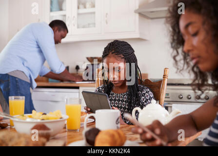 Family Sitting Around Breakfast Table Using Digital Devices Stock Photo