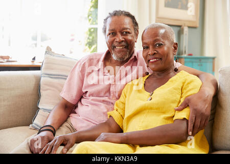 Portrait Of Smiling Senior Couple Sitting On Sofa At Home Stock Photo