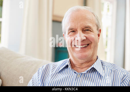 Portrait Of Smiling Senior Man Sitting On Sofa At Home Stock Photo