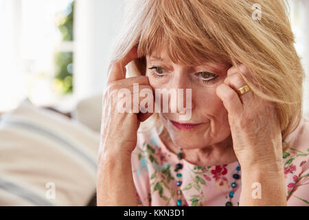 Senior Woman Sitting On Sofa At Home Suffering From Depression Stock Photo