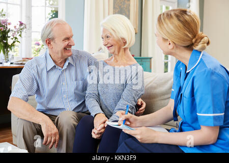 Female Community Nurse Visits Senior Couple At Home Stock Photo