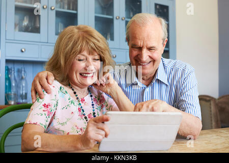 Senior Couple Sit At Home Using Digital Tablet Together Stock Photo