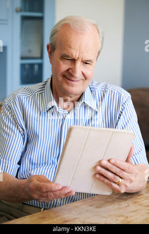 Senior Man Sitting At Home Using Digital Tablet At Table Stock Photo