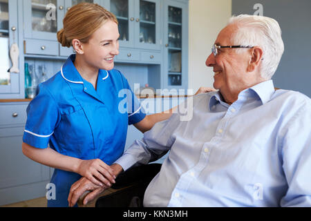 Nurse Talking With Senior Man Sitting In Chair On Home Visit Stock Photo