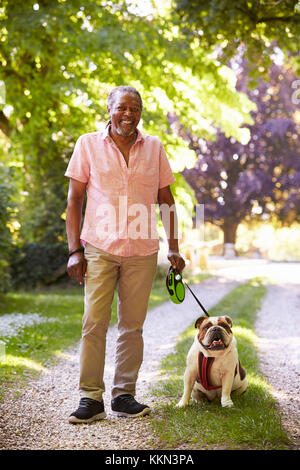 Portrait Of Senior Man Walking Pet Bulldog In Countryside Stock Photo