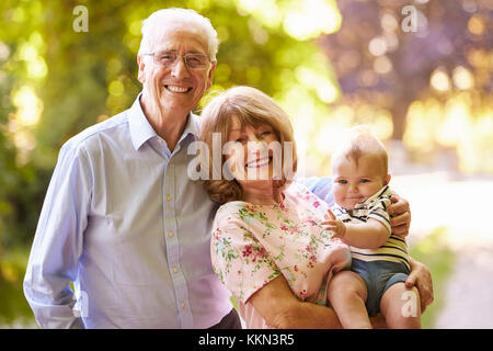 Portrait Of Grandparents Walking In Outdoors With Baby Grandson Stock Photo