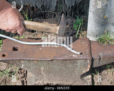 Straightening metal aluminum rod on old rusty anvil with hammer Stock Photo