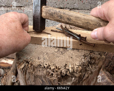 Hands straightening curved nails with hammer on wooden board as anvil Stock Photo