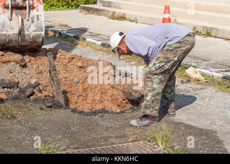 Plumbing Repair Man and excavator scoop digging,  Worker using a small tracked excavator to dig a hole to fix a water on road, and soft-focus backgrou Stock Photo
