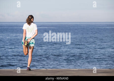 Rear view of female jogger stretching overlooking the sea. Stock Photo