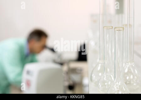 Empty glass flasks in the laboratory and man looking through a microscope. Concept: Research Stock Photo