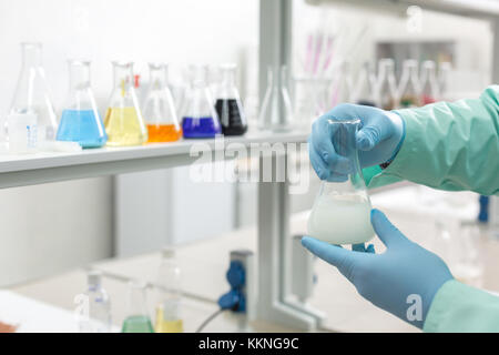 Hands in latex gloves holding flasks on the background of the shelves in the laboratory. Concept: Scientific research Stock Photo