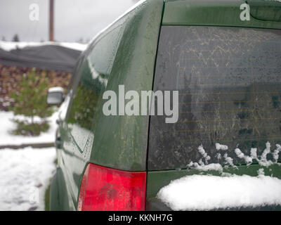 Car rear covered with snow and a firewood stack with chimney in the background Stock Photo