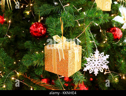 Gold glitter square mini gift box with other colorful Christmas ornaments on a sparkling Christmas Tree Stock Photo