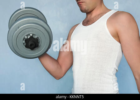 Handsome power athletic man in training pumping up muscles with dumbbell. Simple not a sports not muscular guy shakes her big biceps dumbbells. Home e Stock Photo