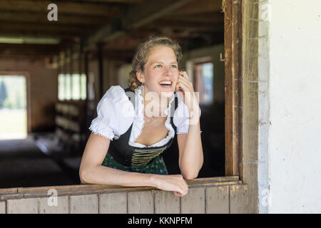 Countrywoman with dirndl looks out of a barn door Stock Photo
