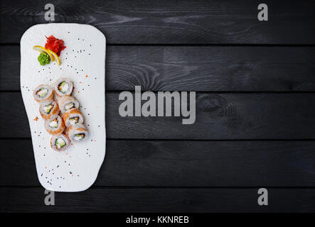 Philadelphia roll with a cucumber, avocado, some cream cheese, tobiko caviar and shrimp. Top view. Black wooden background. Stock Photo