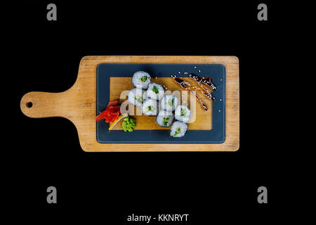 Classic sushi roll with cucumber on a wooden board. Top view. Isolated on a black background Stock Photo