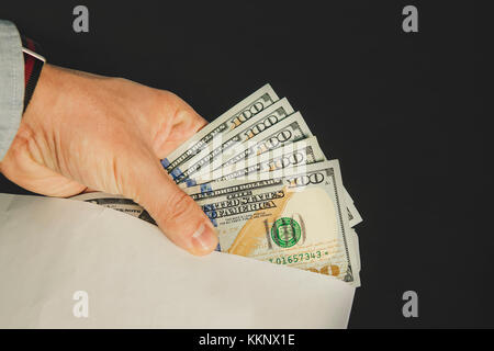 Closeup of man's hands with envelope full of dollar banknotes on wooden background. Concept of corruption and bribery. Illegal remuneration. Tax evasi Stock Photo