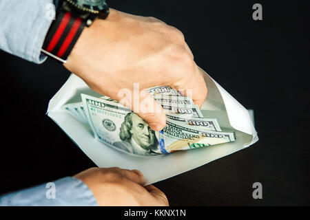 hands of grafter. He take US dollars from white envelope. Bribe-taker the brown wooden table. The employee believes illegal payment in a white envelop Stock Photo