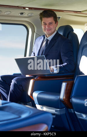 Portrait Of Businessman Working On Laptop In Helicopter Cabin During Flight Stock Photo