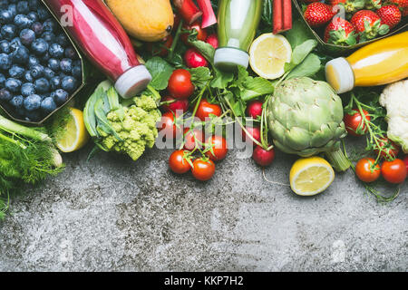 Various colorful smoothie and juices in bottles with fresh organic vegetables and fruits on grey concrete background, top view, border Stock Photo