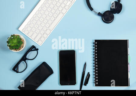 Top view business and freelance items: keyboard, smartphone, pen, glasses, succulent, keyboard on blue background Stock Photo