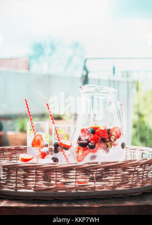 Berries Infused water with ice cubes in jug on tray at outdoor nature background, front view Stock Photo