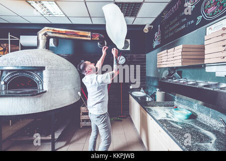 Bearded pizzaiolo chef lunching dough into air. Stock Photo