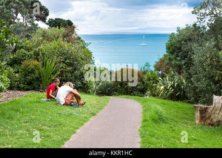Two people sitting on the grass in Waiheke Island, New Zealand Stock Photo