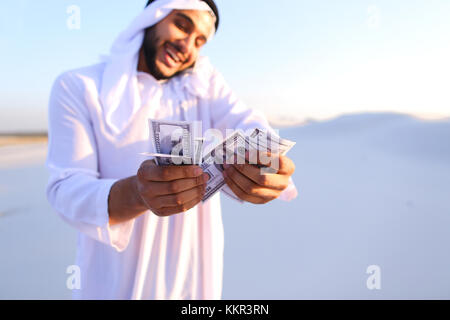 Arab young sheikh calls to friend or business partner and with smile on face and joy in eyes tells about winnings and amount of money in hands, rejoic Stock Photo