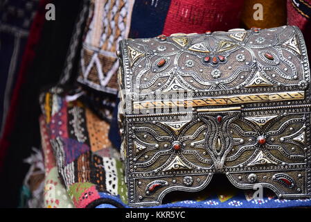Ornate silver trinket box with colorful textiles on sale in a Moroccan Marke Stock Photo