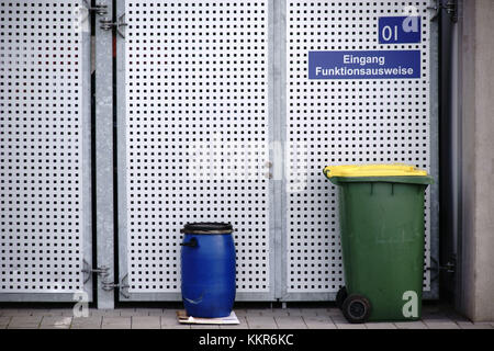 Waste containers standing in front of a (paled) gate made of perforated metal plate. Stock Photo