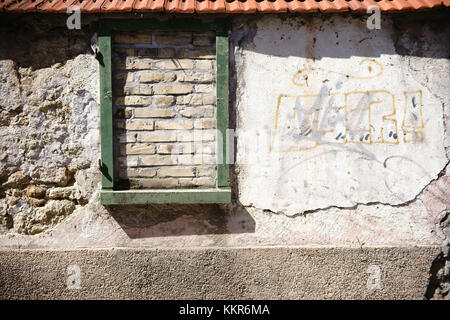 A rustic wall staggered and broken stones with roofing tiles and a bricked up window frame. Stock Photo