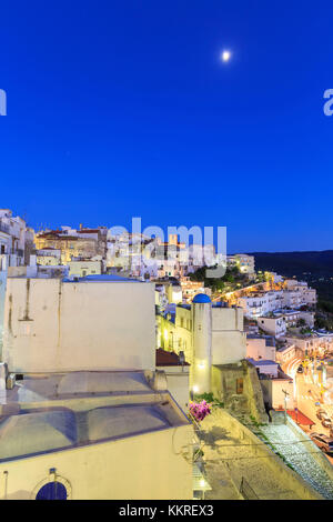 Lights on in the old town of Peschici with the moon in the sky during twilight. Apulia(Puglia), Italy. Stock Photo