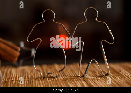 Cookie cutters for gingerbread woman and man standing on straw tablecloth, dark background with bokeh Stock Photo