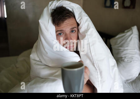 Caucasian male with lack of sleep because he has flu stting in bed and ask for water or medicine Stock Photo