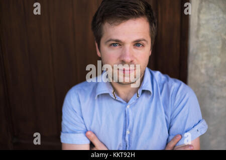 Caucasian man in blue shirt standing near wall and smile a little. He is content and confident. Consept of leadership and self employee Stock Photo
