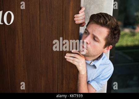 Young caucasian man with agoraphobia spying and looking out the door. Stock Photo