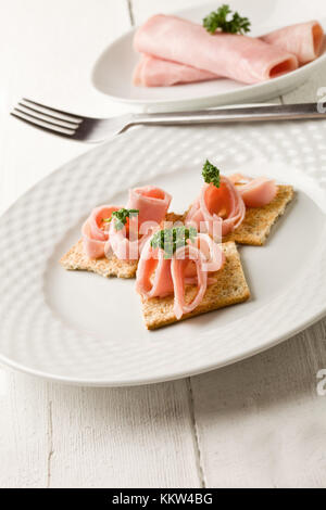 photo of cracker appetizer with  ham and parsley on white wooden table Stock Photo